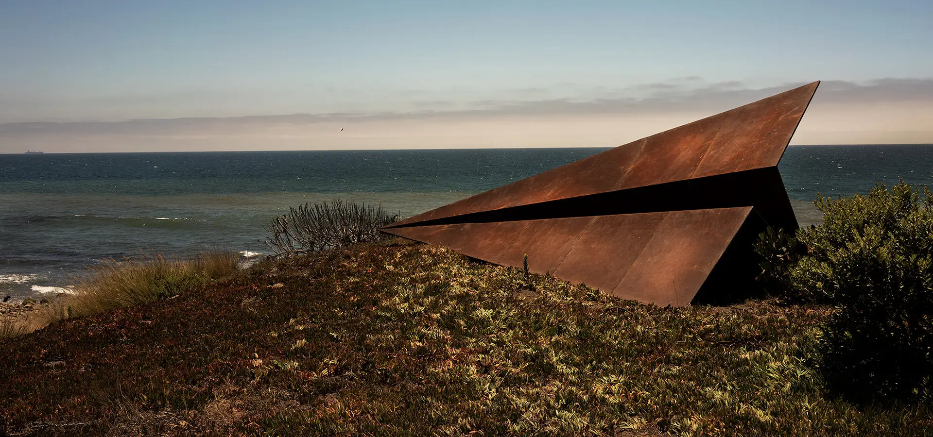 Launch Intention 25ft Metal Paper Plane sculpture in Malibu California on a grassy hill with the Pacific Ocean in the background.