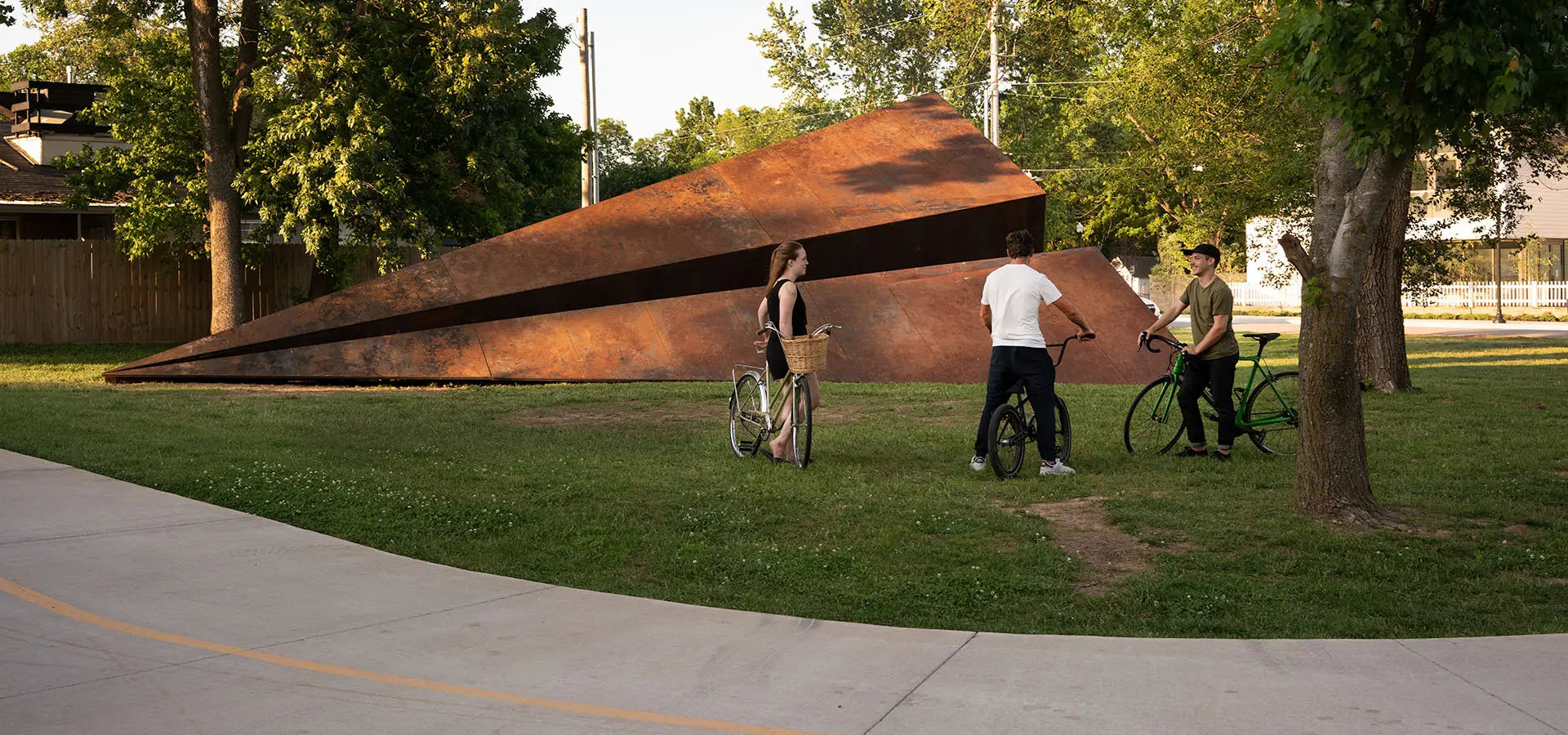 People on bikes around the 50ft Launch Intention Paper Airplane Sculpture in a park in Bentonville, Arkansas downtown.
