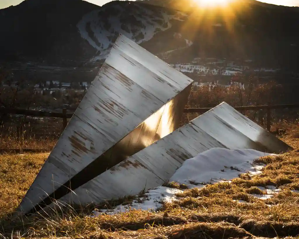 Metal Paper Airplane sculpture in a natural landscape with mountains and sun in Aspen, Colorado.
