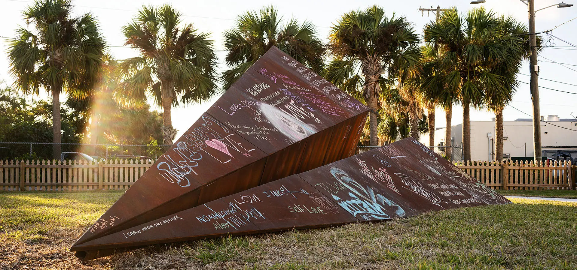 Launch Intention metal paper airplane sculpture sits in front of a group of plan trees during Canvas Outdoor Museum Festival in Palm Beach, Florida.