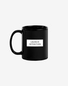 Left side of black Launch Intention staple coffee mug with paper plane branding