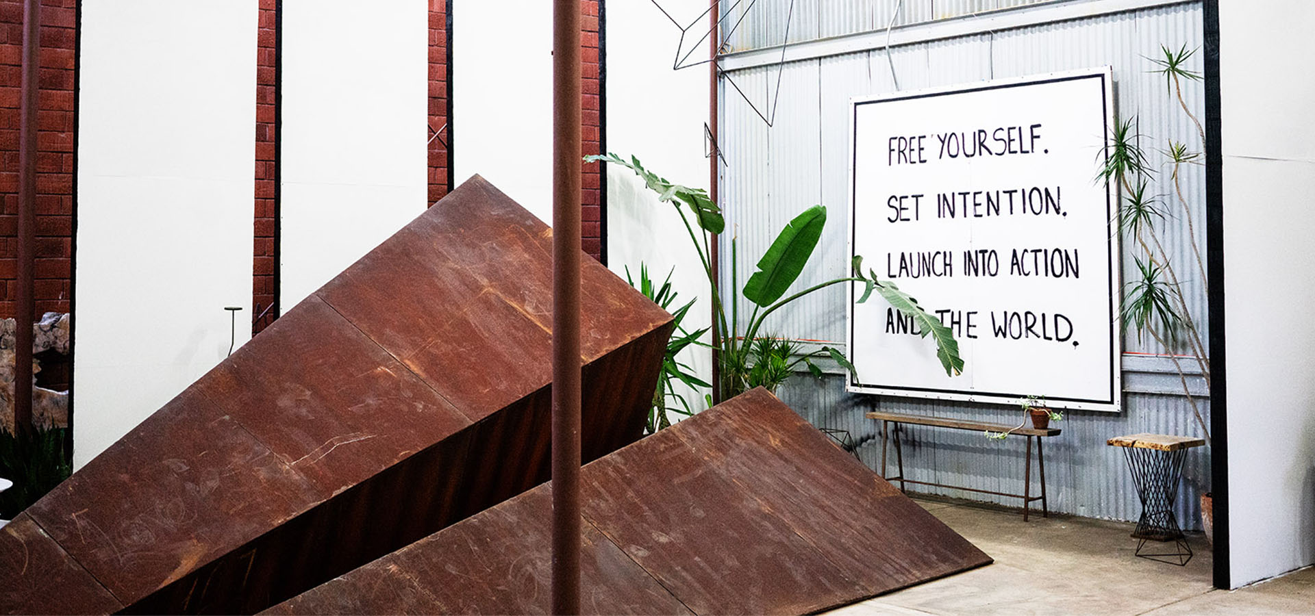 A Launch Intention 25ft Metal Paper Airplane sculpture indoors the VIA studio in front plants of a sign reading "Free Yourself. Set Intention. Launch Into Action and the World."