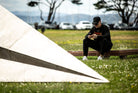Person sitting on a bench in front of the Launch Intention 25 Ft Paper Airplane sculpture on the Marina Green Triangle.