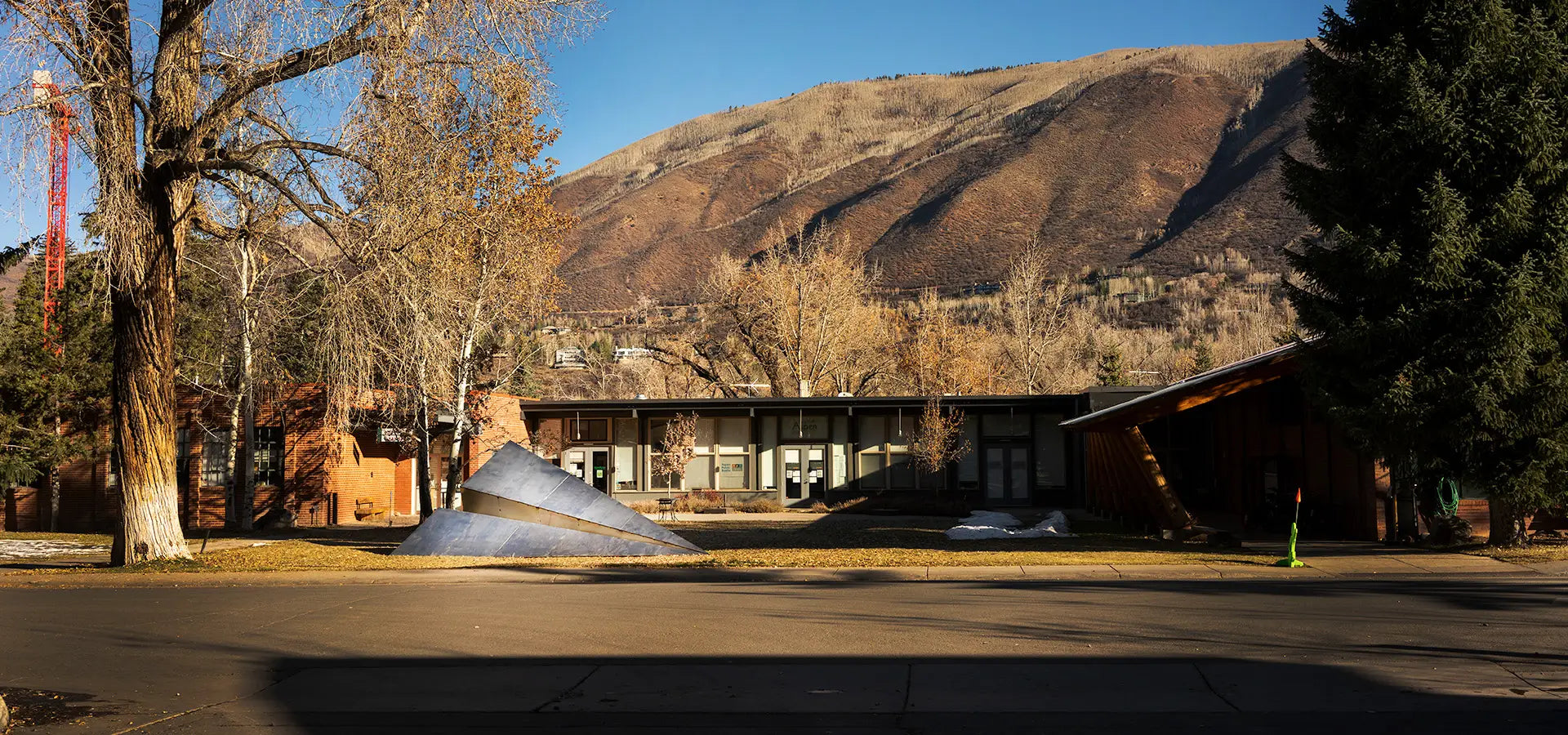 Large Launch Intention metallic paper airplane sculpture in front of the Red Brick School with Red Mountain rising in the background in Aspen, Colorado for Aspen Art Week.