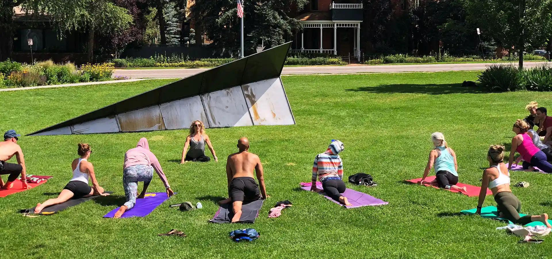 Group of people practicing yoga at Paepcke Park in Aspen Colorado with a modern Launch Intention Paper Airplane sculpture in the background.