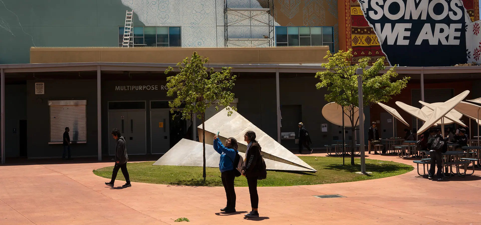 The Dr. Maya Angelou Mural Festival activation of Launch Intention's Metal Paper Plane sculpture in the courtyard of the Community High School in Los Angeles, California with students taking selfies in the foreground.
