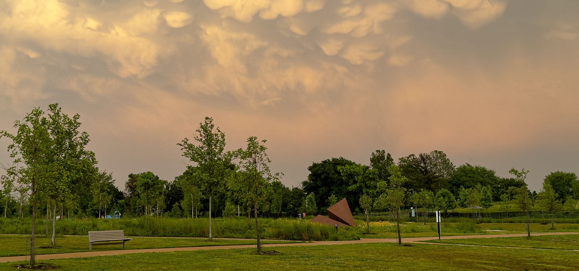  Launch Intention paper airplane sculpture anchored in the meadow at Osage Park beneath dramatic storm clouds, large-scale outdoor artwork symbolizing hope and grounded intention 