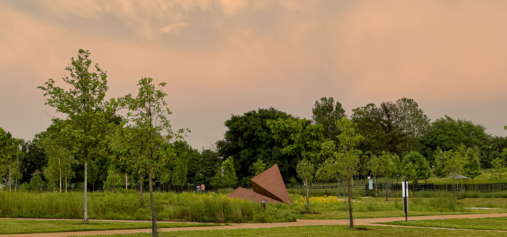  Wide landscape view of Griffin Loop’s Launch Intention paper airplane sculpture at Osage Park under glowing stormy skies, public art beacon for mindful community gathering 