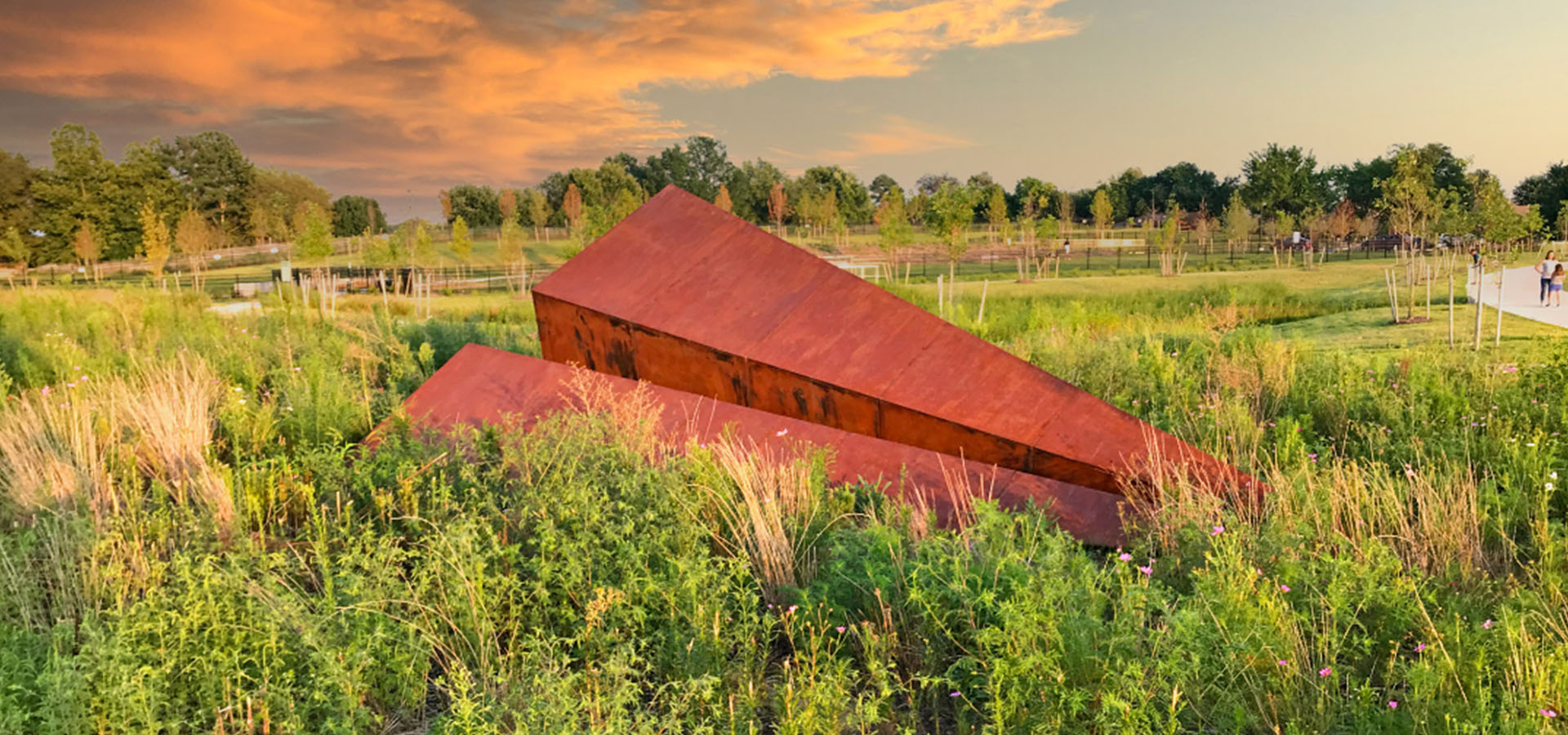 Rust-colored Launch Intemtion Paper Airplane Sculpture in a natural setting with trees and sky at Osage Park In Arkansas