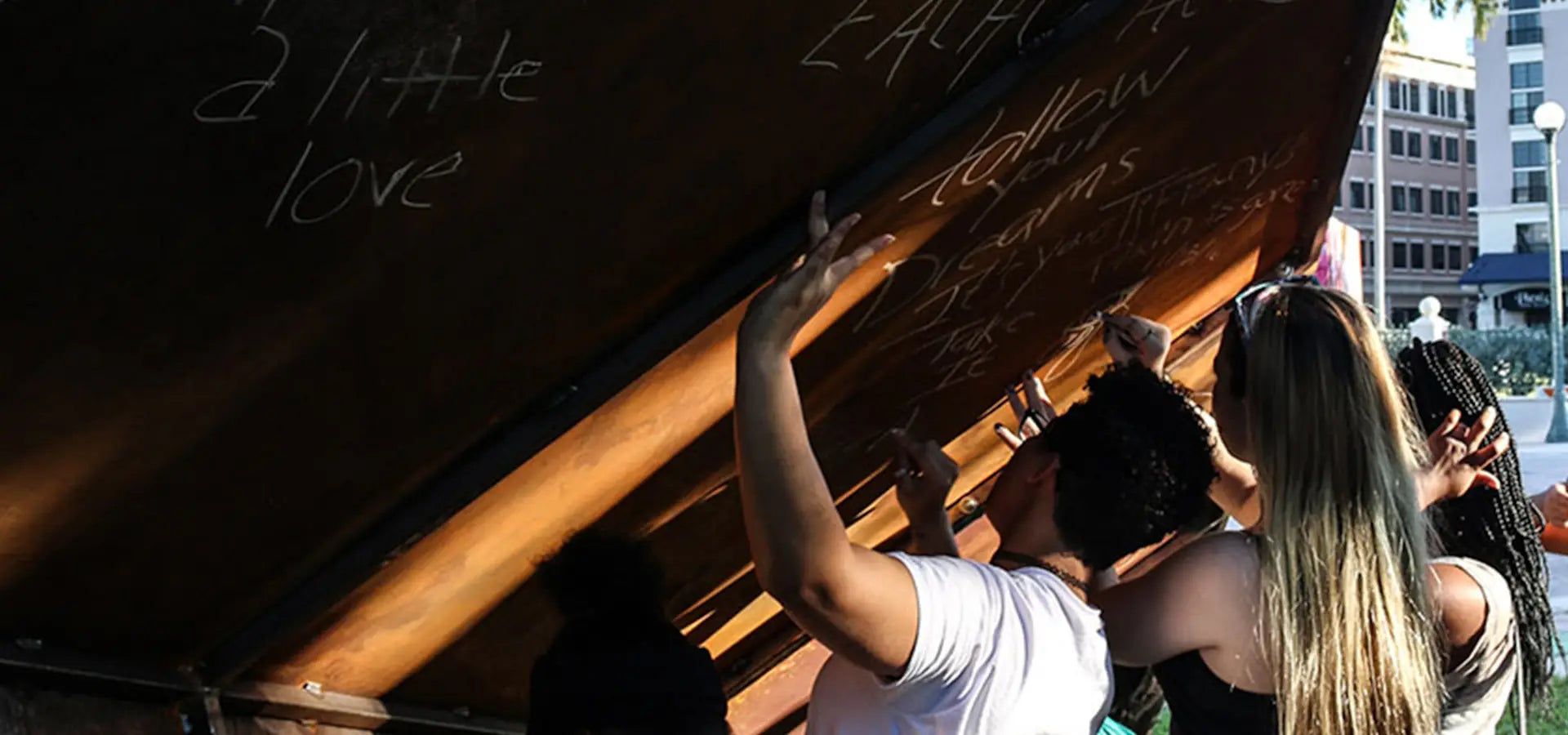 People interacting with a large metal paper airplane sculpture outdoors, writing their intentions on it for the Launch Intention project at the Canvas Outdoor Museum.