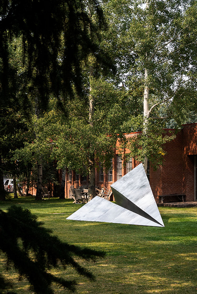 Modern Paper Airplane sculpture on grass with a brick building and trees in the background at the Red Brick School in Aspen, Colorado.