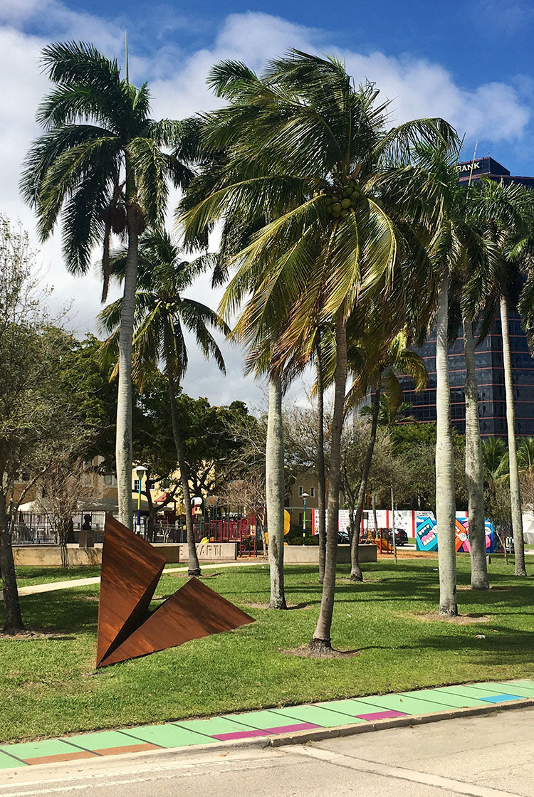 A Metal Paper Airplane sculpture in a Florida Park with palm trees, a colorful pathway during the Canvas Outdoor Museum Festival.