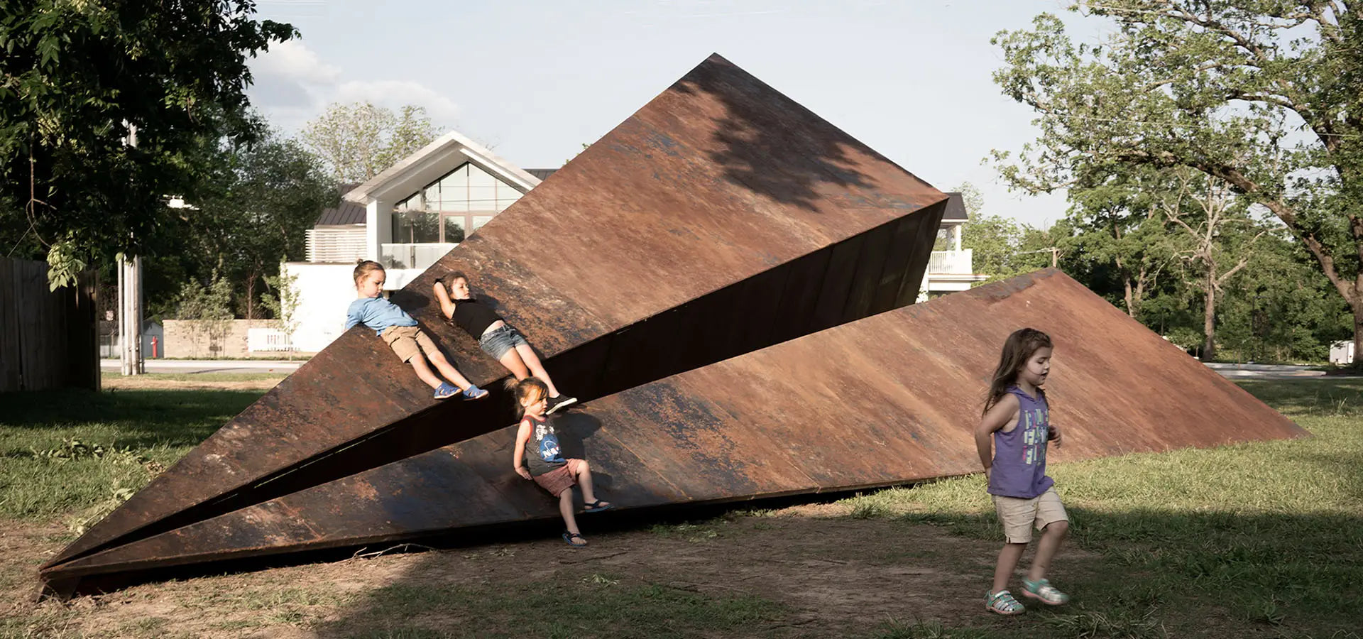 Kids playing on Launch Intention's large 50 foot metal paper airplane sculpture in a Bentonville Arkansas park in front of the Blake Street building.