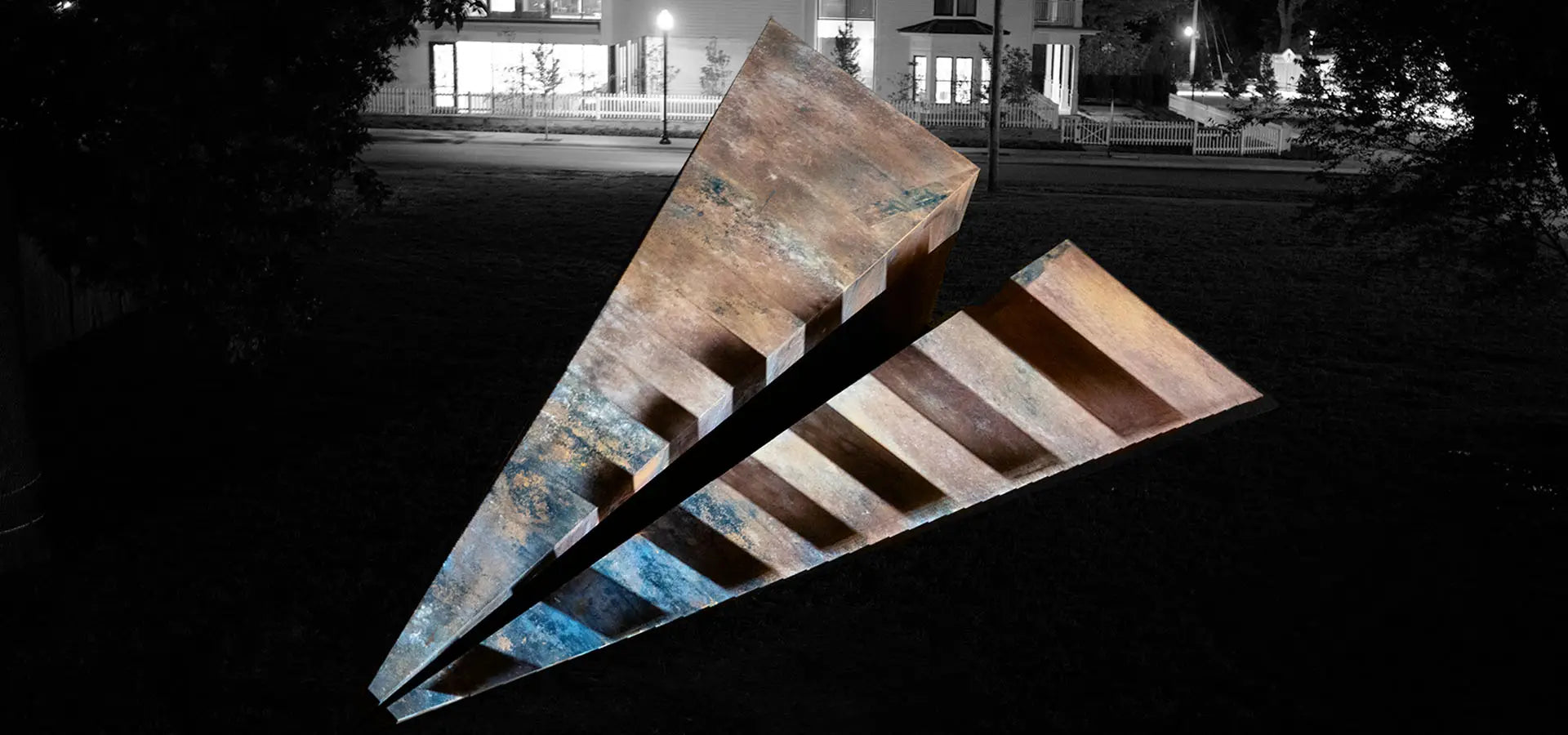 Black and White striped Launch Intention's large 50 foot metal paper airplane sculpture in a Bentonville Arkansas park in front of the Blake Street building at night during a projection mapping activation.