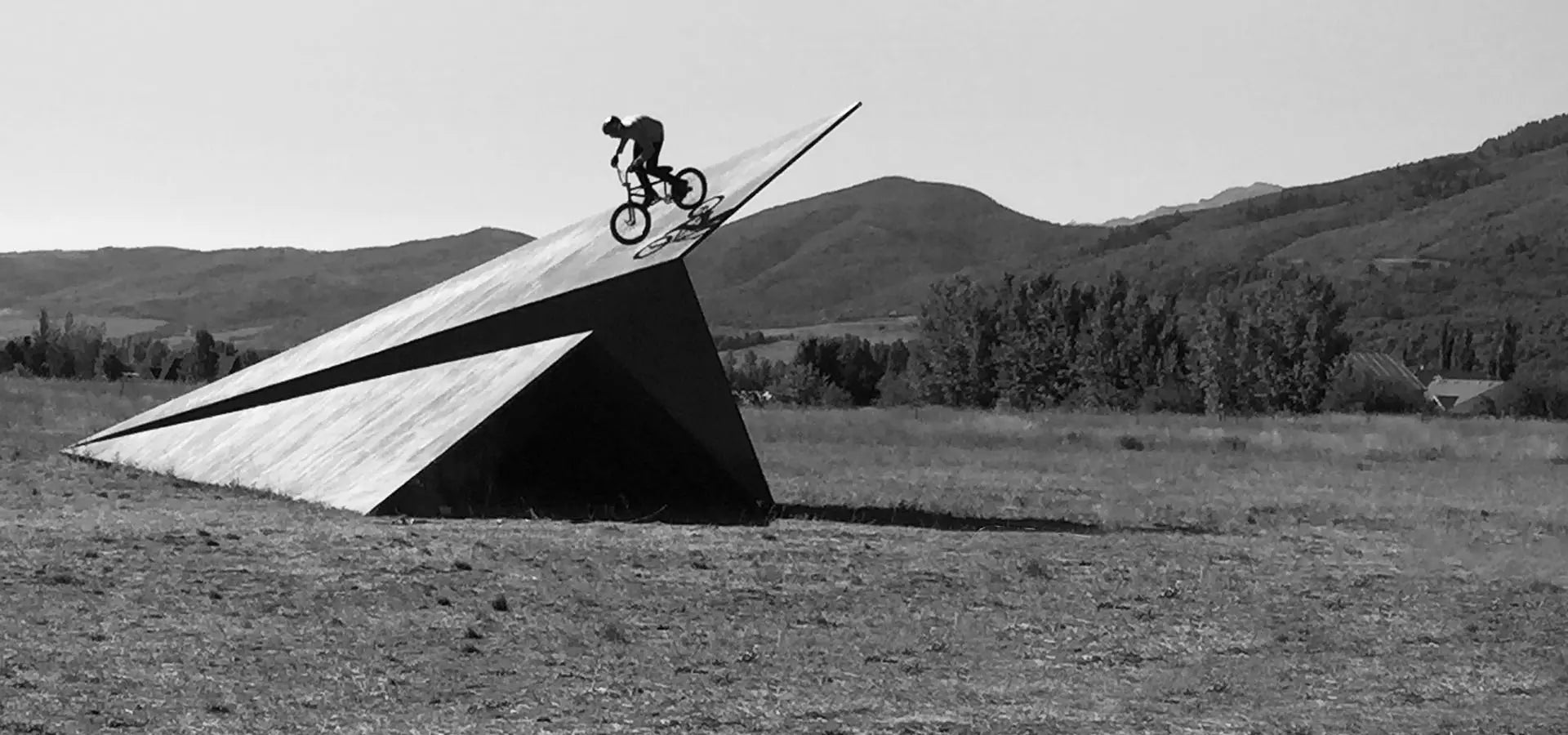 Person on a bicycle performing a trick on a Launch Intention 50ft paper airplane sculpture with Utah mountains in the background.