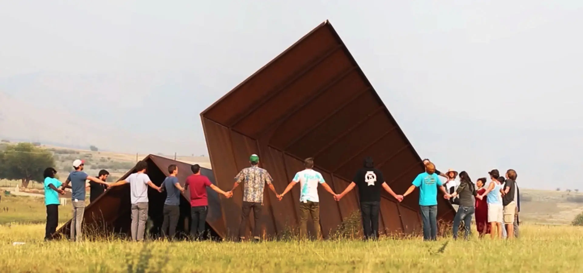 Group of people holding hands in front of Launch Intention's large metal paper airplane sculpture in a field at Powder Mountain, Utah.