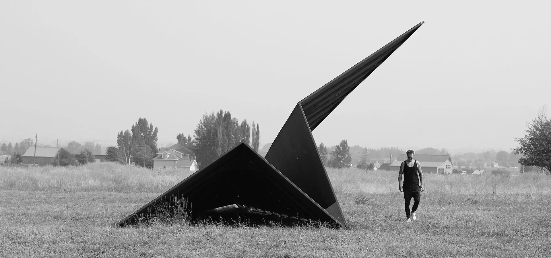 Artist Griffin Loop walking towards a large metal paper airplane sculpture in an open field at Powder Mountain, Utah.