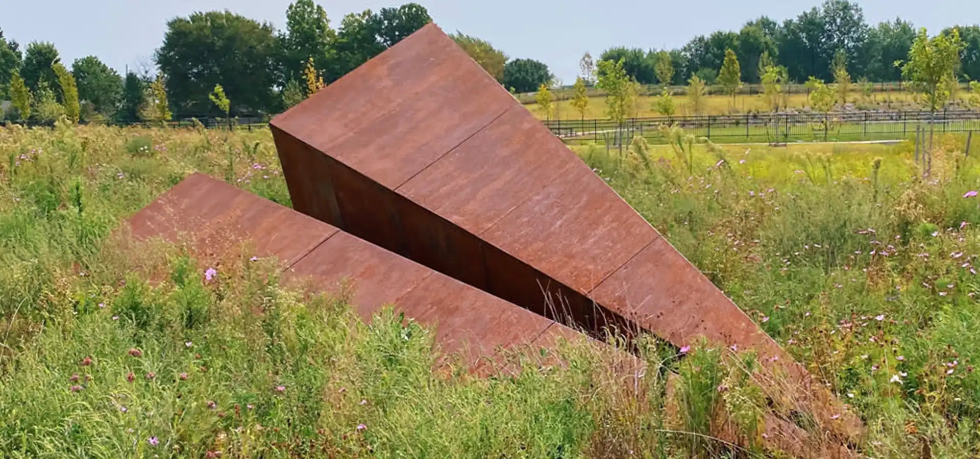 Launch Intention large scale 25 foot paper airplane sculpture rests in Osage Park Arkansas surrounded by wildflowers and green trees.