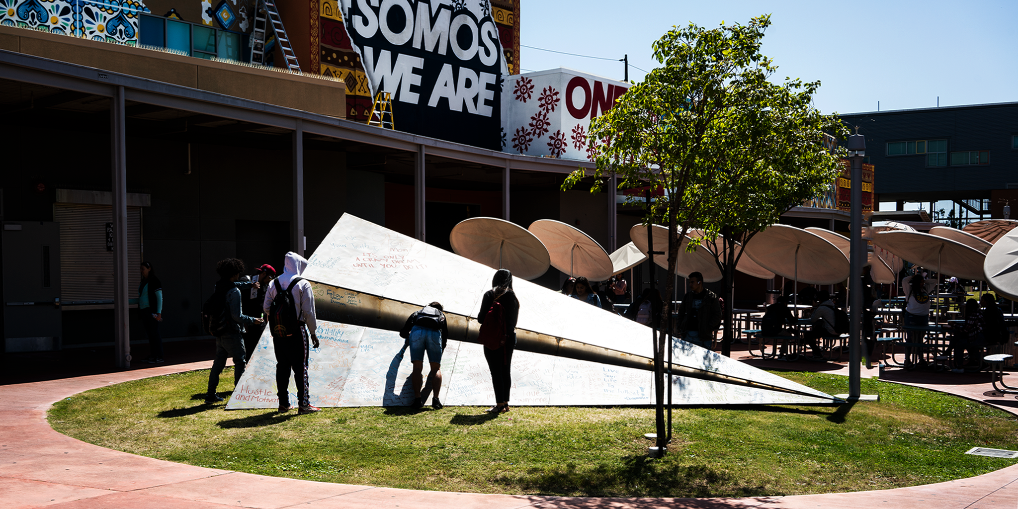 The Dr. Maya Angelou Mural Festival activation of Launch Intention's Metal Paper Airplane sculpture in the courtyard of the Community High School in Los Angeles, California with students writing intentions on the wing in the foreground.