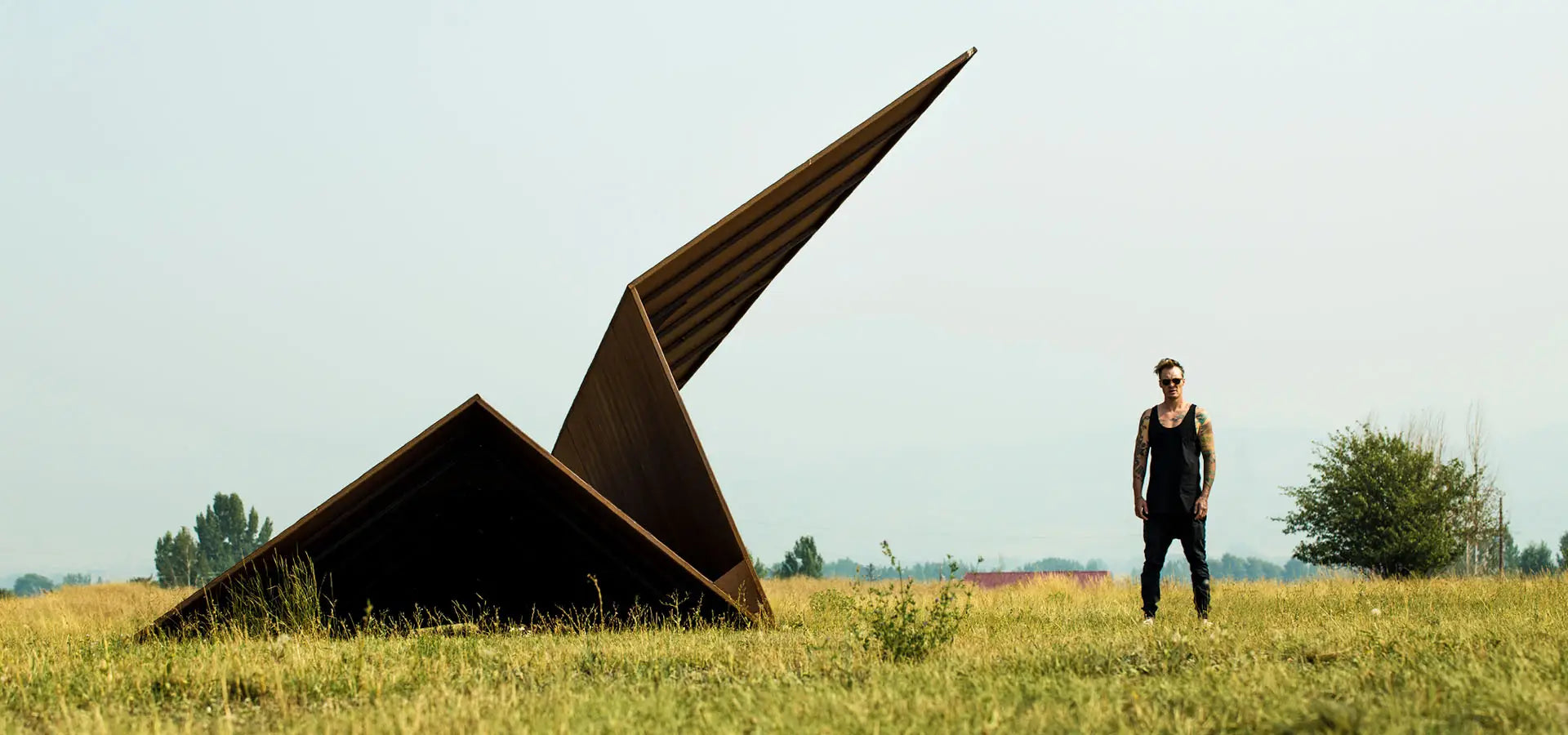 Artist & Founder Griffin Loop standing next to his large metal paper airplane sculpture in an open field at Powder Mountain, Utah for the first Launch Intention Community Activation.
