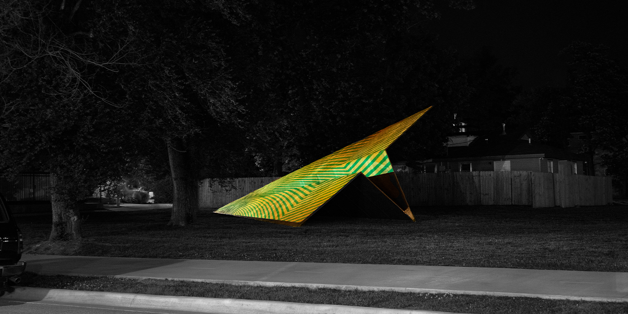 Yellow and Green projection mapped striped Paper Airplane sculpture from Launch Intention on a black and white park background.