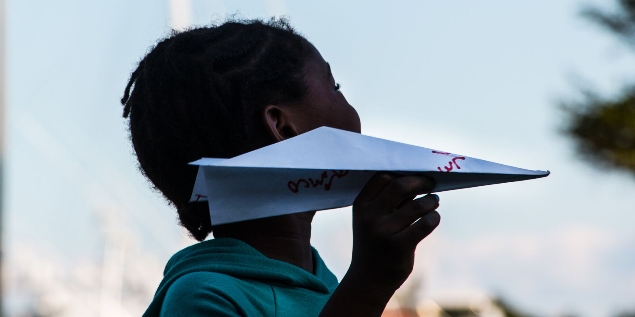 A person throwing a paper airplane with an Intention written on it against a blurred outdoor background at a Launch Intention activation.