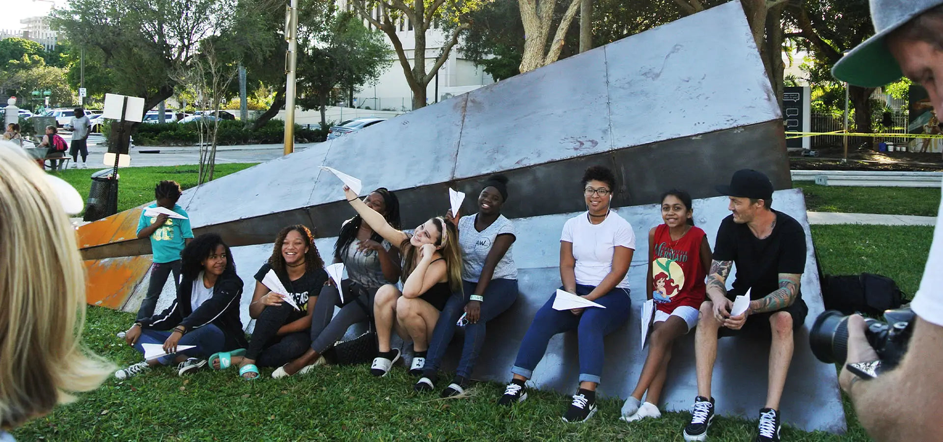 Group of people sitting on a large launch intention paper airplane sculpture at the Canvas Outdoor Museum in Palm Beach, Florida.