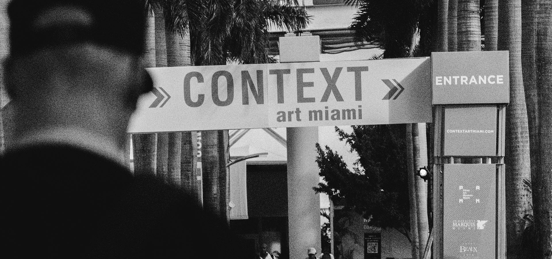 Entrance sign for Context Art Miami event with artist Griffin Loop walking in the foreground.