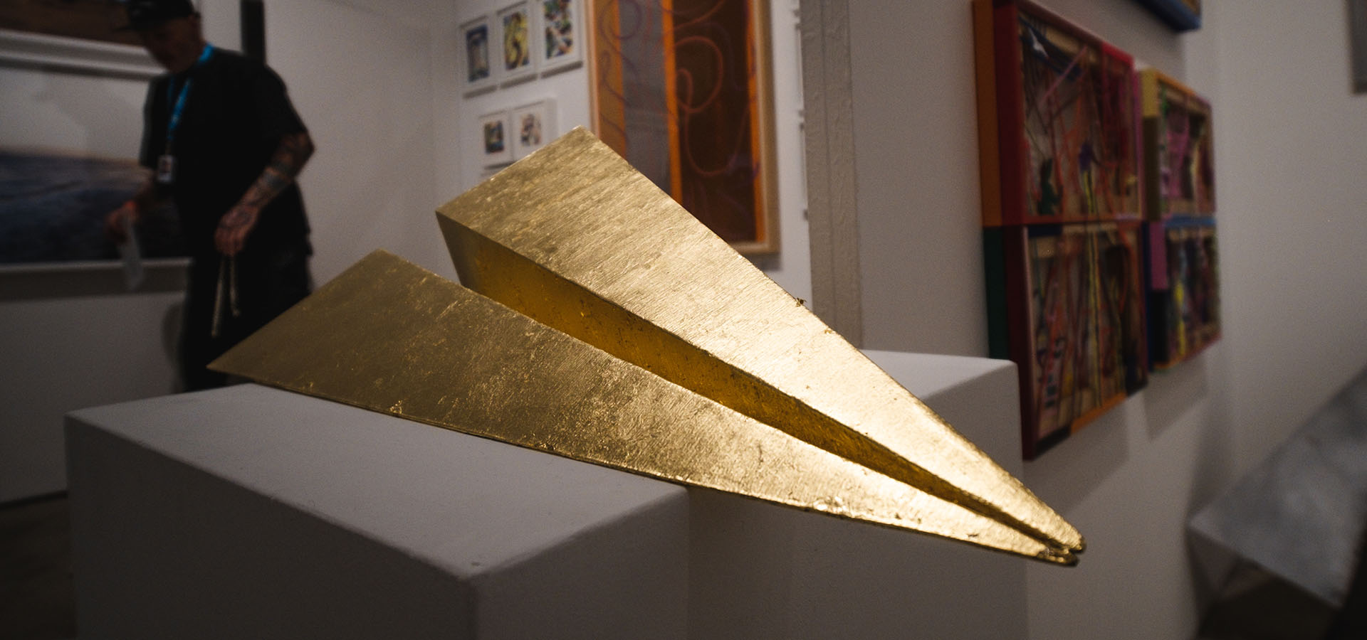 Launch Intention's Gold paper airplane sculpture on a white pedestal at Context Art Miami during Art Basel.