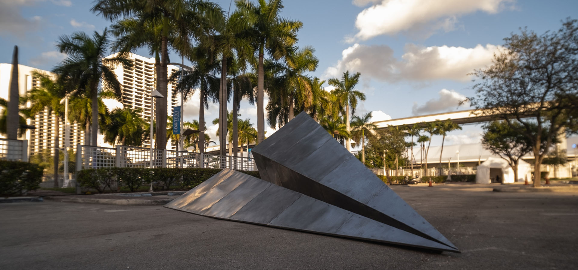 Launch Intention metal paper airplane sculpture sits in front of a group of palm trees at the enterance of Context Art Miami, in Florida during Art Basel.