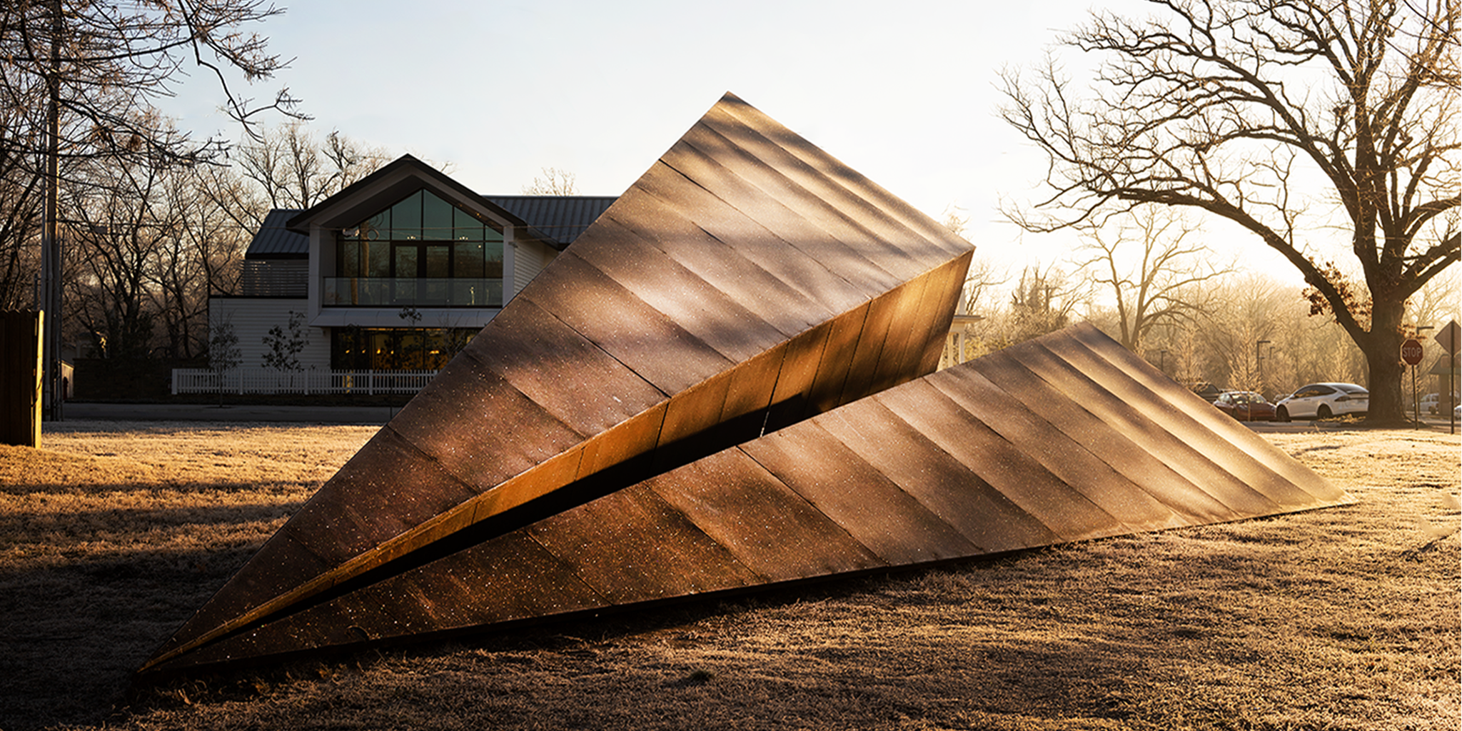 Rusted Launch Intention Paper Airplane geometric sculpture in a Bentonville Arkansas park with trees and a building in the background.