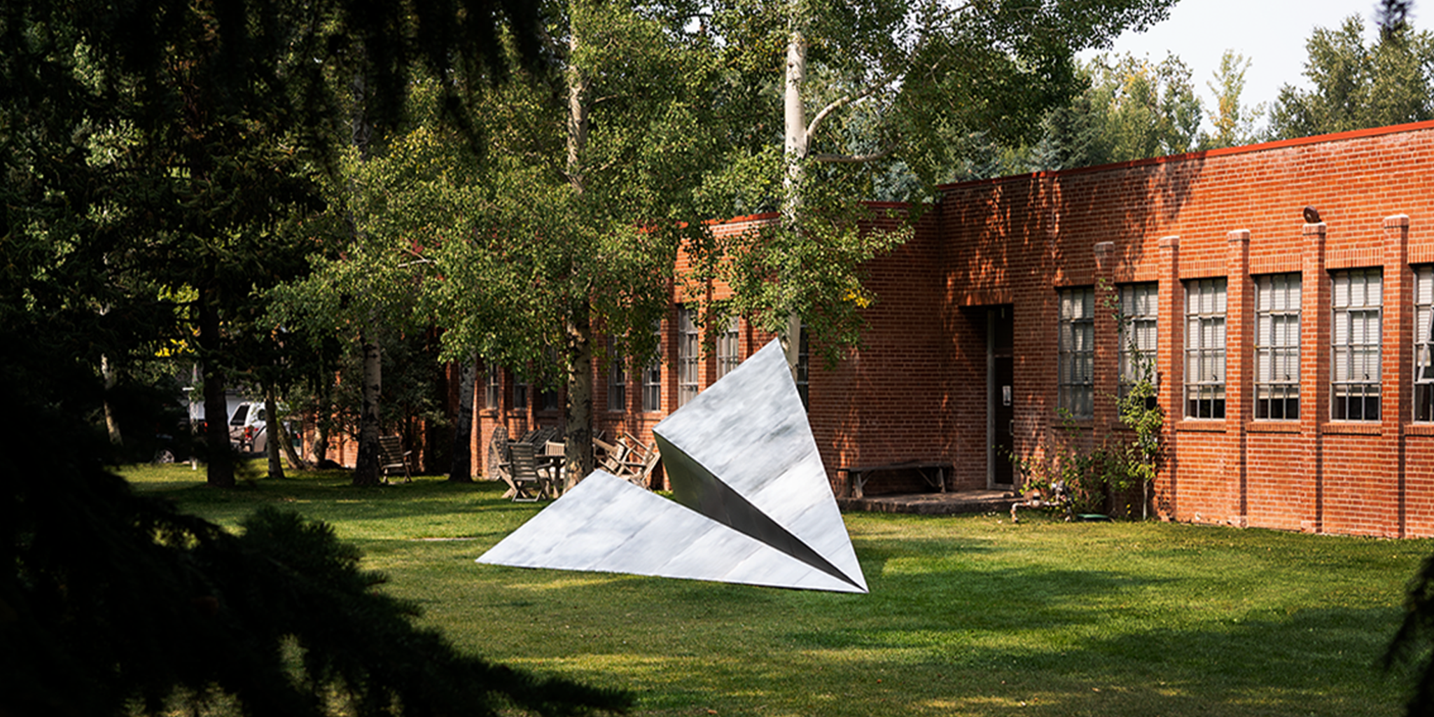 Modern Paper Airplane sculpture on grass with a brick building and trees in the background at the Red Brick School in Aspen, Colorado.