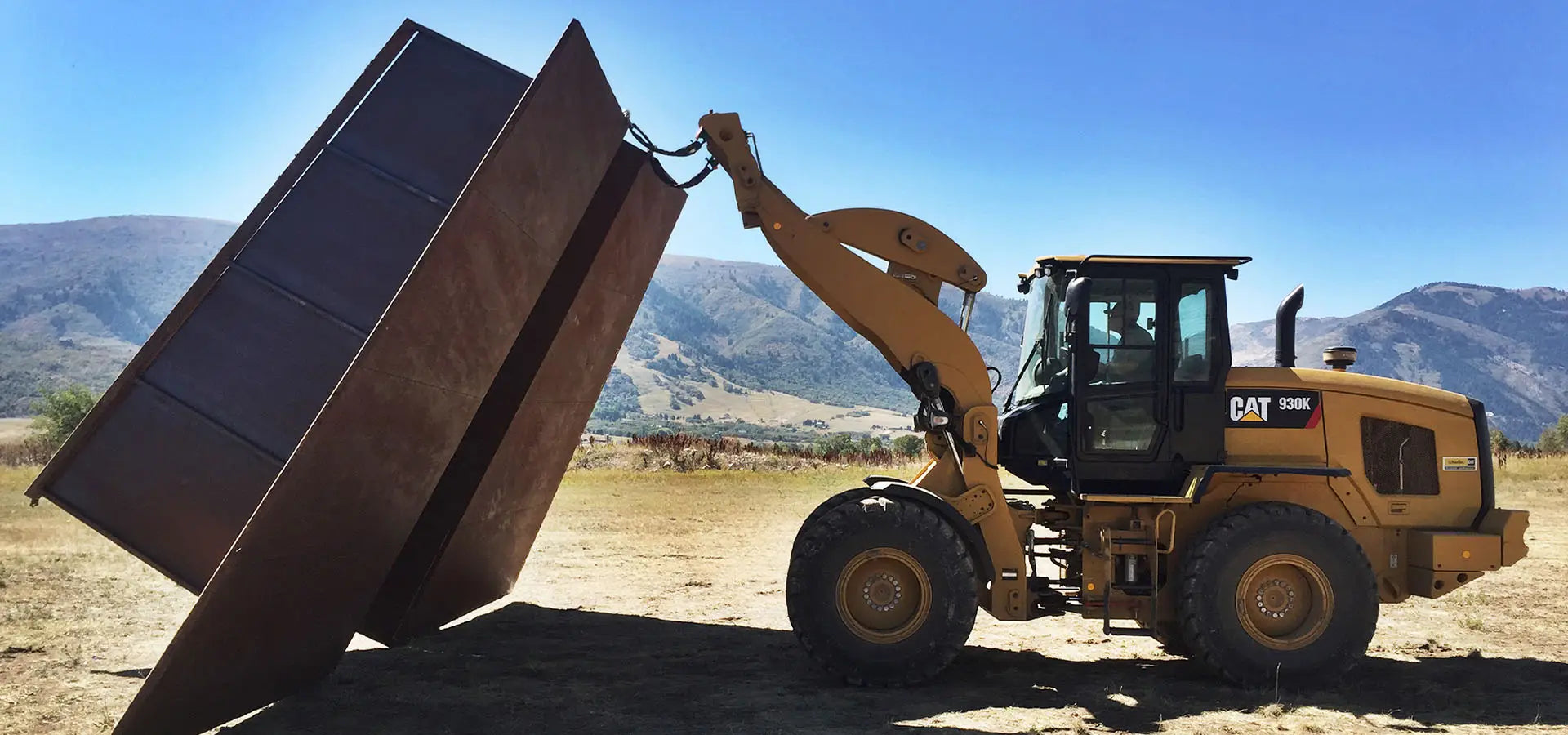 Yellow Caterpillar bulldozer with large metal bucket in the Eden Valley of Powder Mountain Utah installing the rear section of a Launch Intention Paper Airplane sculpture.