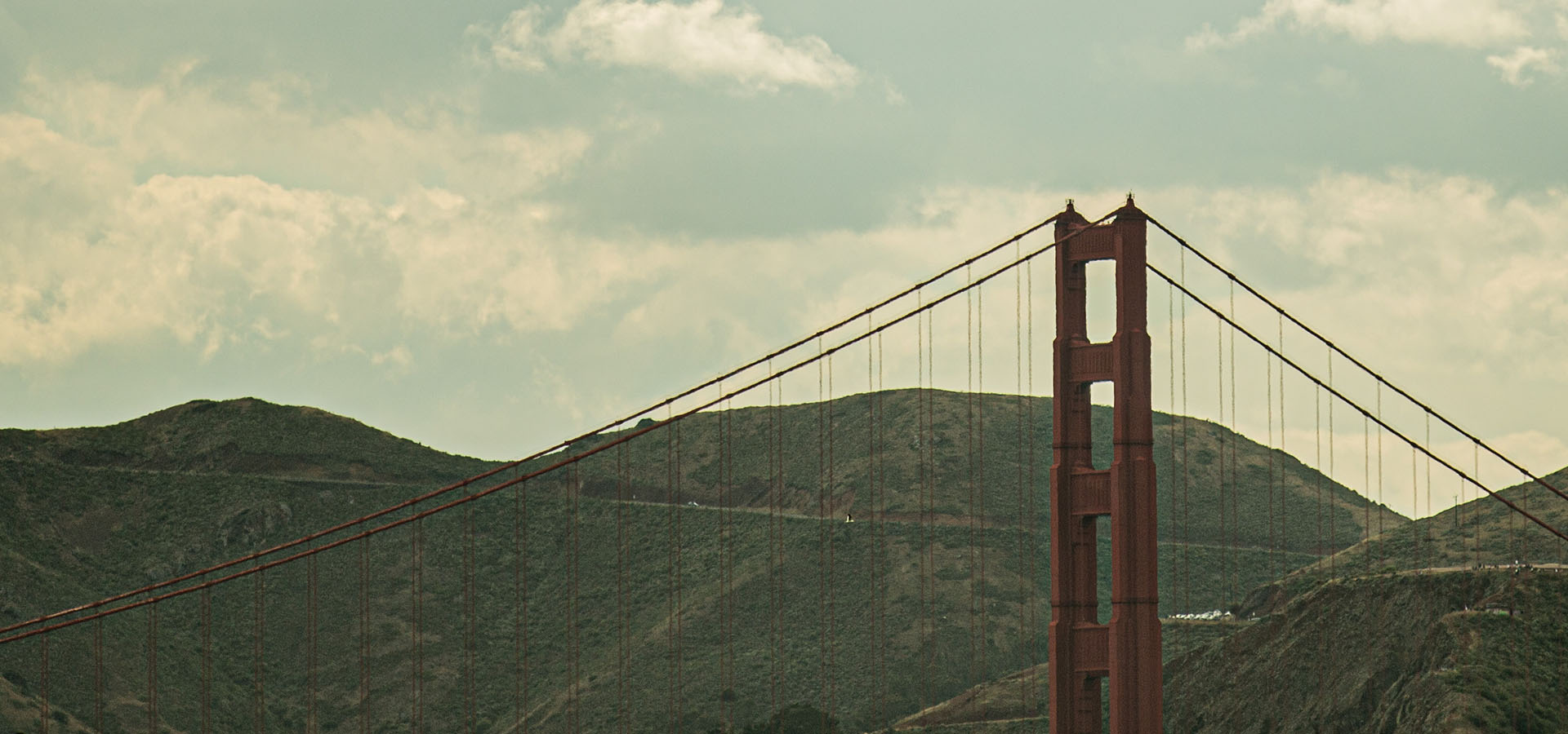 View of The Golden Gate Bridge from the Launch Intention 25 Ft Paper Airplane sculpture on the Marina Green Triangle park with mountains in the background.
